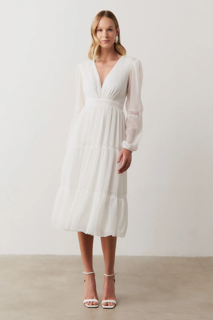 Modelo usando vestido midi fluido com manga longa e decote V Manu Off White da Koji, elegante para mãe e madrinha de batizado na igreja