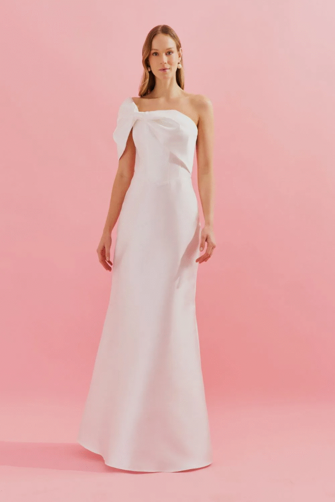 Modelo usando vestido longo estruturado de um ombro só com laço Lima Off White da Koji, ideal para noiva de casamento civil moderna